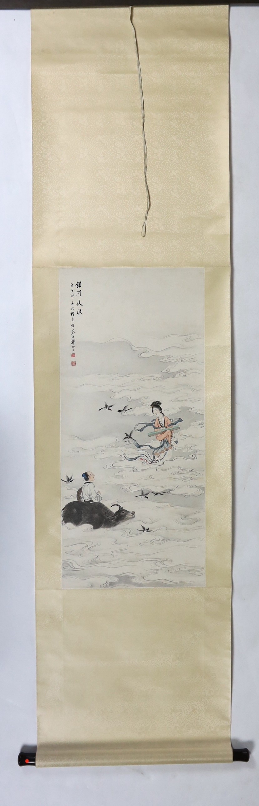 A Chinese scroll painting on paper of a female immortal and a male immortal riding a Buffalo amid clouds and birds, early 20th century, image 77cm x 34.5cm